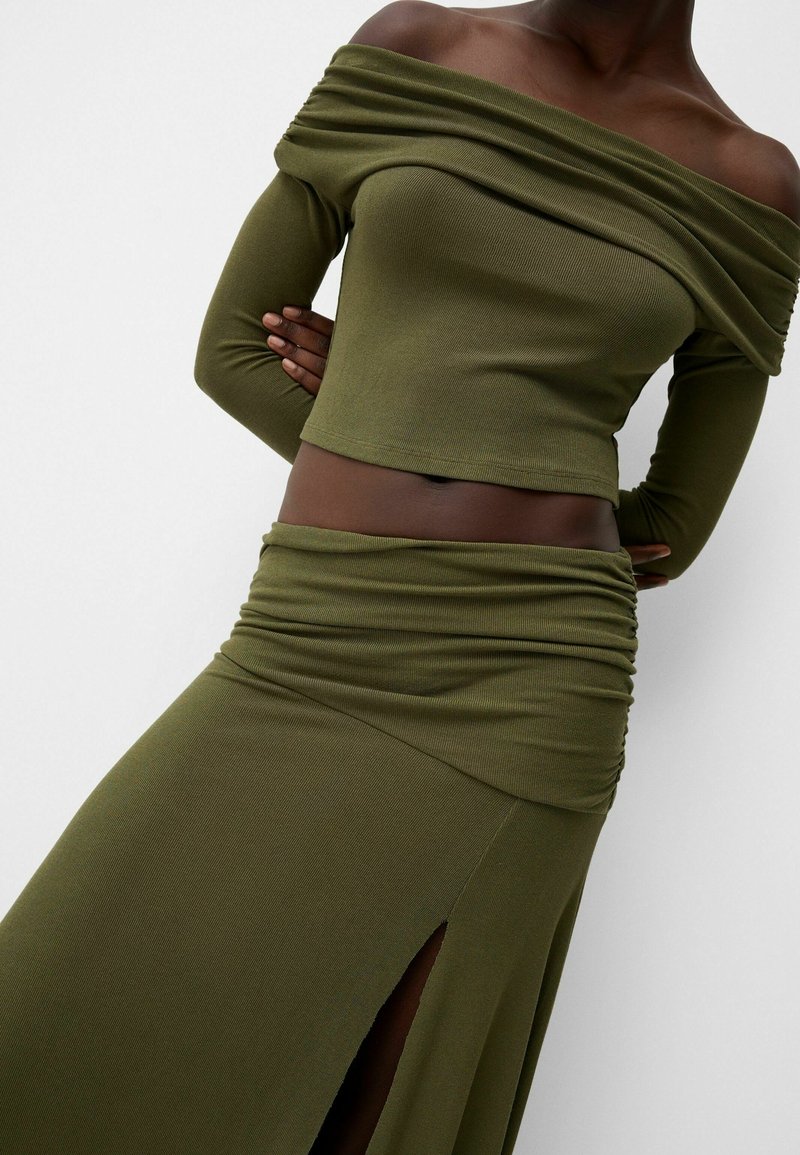 Haut olive décolleté avec des manches longues et une jupe assortie présentant une texture plissée et une fente haute sur la cuisse.