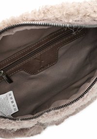 Interno della borsa in pelliccia sintetica beige, con una tasca in pelle marrone dotata di zip. Fodera in tessuto marrone e etichetta di cura attaccata nella parte inferiore.