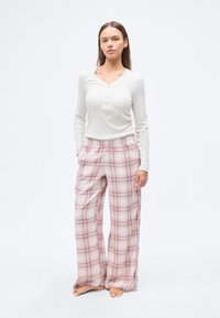 Μπεζ μπλούζα henley με μακριά μανίκια και τρία κουμπιά· φαρδιά παντελόνια με ροζ-ανοιχτό καρό, ελαστική μέση και πλαϊνές τσέπες.