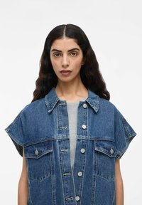 Denim žakete ar īsām piedurknēm, gaiši zila krāsā, priekšējā pogu aizdare, divas krūšu kabatas un kontrastējoši šuvieni.