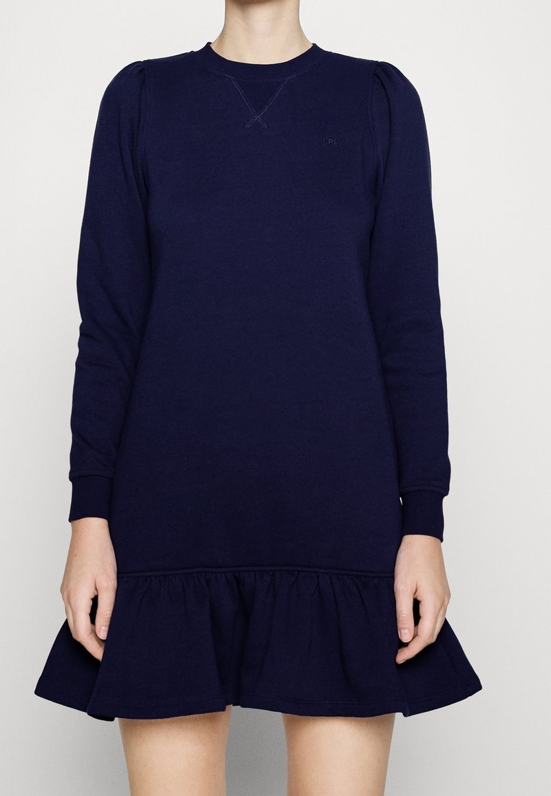 Navyblå sweatshirtklänning med långa ärmar, ribbade mudd och volangnederdel. Tillverkad av mjukt material och har subtila samlingar vid axlarna.