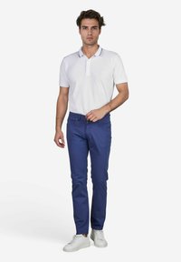 Witte polo met korte mouwen en een kraag, gecombineerd met blauwe slim-fit broek. Het model draagt witte sneakers. Eenvoudig ontwerp, geen patronen.