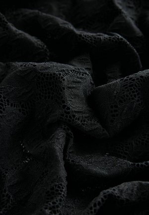 Must räbalise mustrilise pitsiga kude, millel on keerukad lillemustrid ja erinevad tekstuurid, omades pehmet, kortsus välimust.