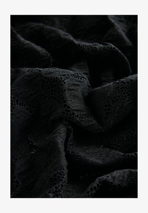 Must räbalise mustrilise pitsiga kude, millel on keerukad lillemustrid ja erinevad tekstuurid, omades pehmet, kortsus välimust.