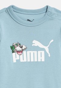 Ανοιχτού μπλε παιδικό πουκάμισο με λευκό λογότυπο Puma, γραφικό με πηδώντας πούμα και μια καρτούν πράσινο ζωάκι με γυαλιά στον εμπρόσθιο μέρος.