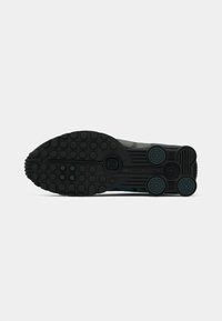 Sole di sneaker nera in gomma testurizzata, con motivi di presa circolari e un design geometrico. Accenti in teal e verde scuro.