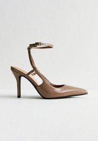 Zapato slingback de punta afilada con un acabado brillante en charol beige, tira del tobillo delgada y tacón de 10 cm, con detalles laterales recortados.