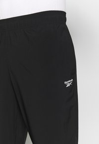 Bermudas atléticas pretas feitas de tecido leve, com uma cintura elástica e um pequeno logotipo branco da Reebok na lateral.