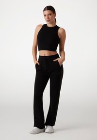Sort ribbet crop top med høj hals, kombineret med sorte sweatpants med sidelommer og elastisk talje. Hvide sneakers fuldender outfittet.