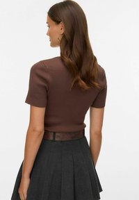 Pruuni soonikkoespritsiga lühikeste varrukatega top, millele on kombineeritud tumehall volditud seelik ja pruun vöö. Lihtne, keha järgnev disain.