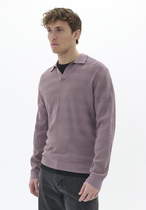 Suéter polo de manga larga de color púrpura claro con un diseño texturizado y cuello abierto, combinado con jeans oscuros, llevado por un modelo frente a un fondo blanco.