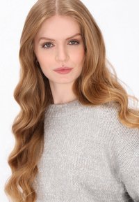 Lichtgrijze gebreide trui met een ronde halslijn, voorzien van een zachte textuur en subtiele glans. Model heeft lang, golvend haar.