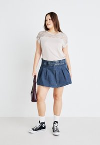 Hellgraues Oberteil mit strukturiertem Spitzenoverlay, kombiniert mit einem dunkelblauen Denim-Minirock mit Falten und schwarzen High-Top-Sneakers, hält eine burgunderfarbene Tasche.