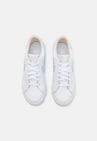 Baskets blanches avec des accents bleu clair, tige en cuir, bout rond, lacets plats et doublure en textile. Logo Nike sur le côté et sur la semelle intérieure.