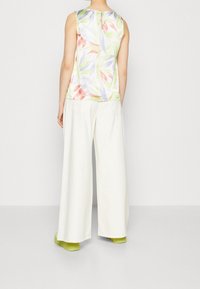 Wielokolorowy top bez rękawów z kwiatowym wzorem, zestawiony z szerokimi białymi spodniami i zielonymi butami. Teksturowana tkanina i luźny krój.