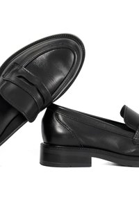 Black leather loafers with a smooth texture, rounded toe, and a decorative strap across the front. Low, solid black heel.