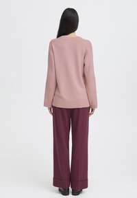 Jasnoróżowy sweter w robocie z ribbowanym dołem, zestawiony z szerokimi burgundowymi spodniami z założonymi mankietami. Prosty, estetyczny design.