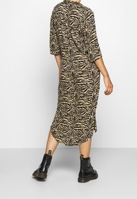 Abito beige con una stampa a zebre nera, lunghezza fino al polpaccio, maniche corte, fessure laterali, abbinato a stivali neri fino alla caviglia.