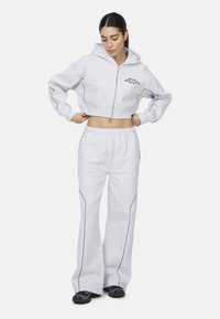 Przycięta szara bluza z kapturem na zamek, z czarnymi szwami. W połączeniu z szarymi spodniami dresowymi, również z kontrastowymi przeszyciami, oraz czarnym obuwiem.