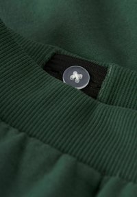 Groene stof met een gemêleerde geribbelde tailleband, met een heldere knop met een kruisontwerp. Close-up detailopname die de stof en kleur benadrukt.