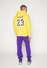 Sweatshirt amarelo com detalhes roxos e grande "23" nas costas, combinado com calças de moletão roxas e sapatilhas pretas com detalhes amarelos.