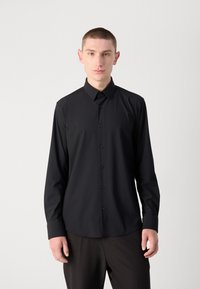 Svart langermet skjorte med klassisk krage, knappelukking foran, og en glatt tekstur. Har en slim fit og mørke knapper langs pløssen.