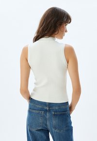 Top blanco de canalé sin mangas con cuello alto, acompañado de jeans azules de talle alto con dos bolsillos traseros.