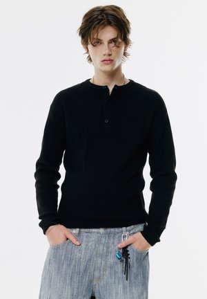 Sort ribbet langærmet henley top med en tre-knaps placket, parret med lyseblå denim jeans med synlige hardware og tilbehør.