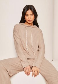 Beige ribbet hættetrøje med snøre, der har en blød tekstur og lange ærmer. Sammen med matchende ribbet bukser. Minimalistisk design.