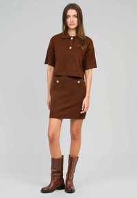 Ensemble deux pièces en laine marron comprenant un haut polo à manches courtes avec col et une jupe ajustée avec des boutons décoratifs et un ourlet côtelé. Bottes en cuir marron.