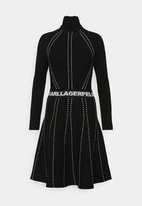 Robe tricot à manches longues noire avec col roulé, ornée de lignes verticales blanches en pointillés et d'une ceinture avec le logo "KARL LAGERFELD" à la taille.