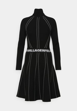 Robe tricot à manches longues noire avec col roulé, ornée de lignes verticales blanches en pointillés et d'une ceinture avec le logo "KARL LAGERFELD" à la taille.