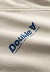 Μπεζ ύφασμα με υφή επιφάνειας που διαθέτει έντονα μπλε γράμματα με την επιγραφή "Double A by WOOD WOOD Copenhagen, Denmark."