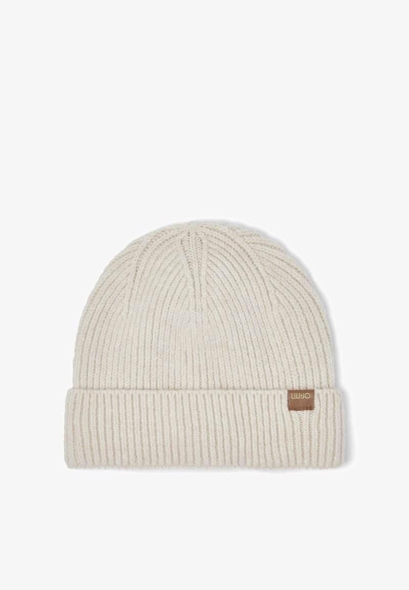 Bonnet tricoté beige clair avec une texture côtelée et une petite étiquette en tissu marron sur le revers plié.