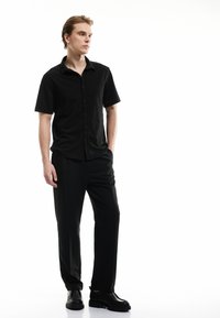 Camicia nera a maniche corte con un motivo testurizzato e chiusura con bottoni. Abbinata a pantaloni neri e scarpe nere eleganti con una suola resistente.