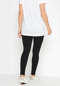 Leggings neri realizzati in materiale elastico, caratterizzati da una vestibilità slim. Abbinati a una maglietta bianca lunga e a sneakers bianche con accenti grigi.