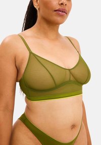 Läpinäkyvä vihreä bralette, jossa on säädettävät olkaimet, leveä vyötärönauha ja vaaleanvihreä kontrastiäri. Yhdistetty vastaavien bikineiden kanssa.