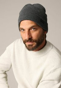 Bonnet gris tricoté avec une texture côtelée et une étiquette, associé à un pull beige crème avec des côtes verticales.