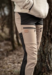 Tan en zwarte outdoor broeken met ritszakken, gemaakt van een gestructureerde stof, met duurzame stiksels en een bruine leren label "SWEDENHUNT."