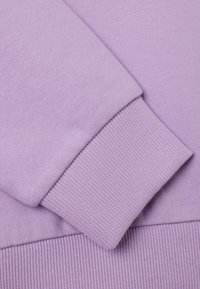 Sudadera lila con puños acanalados, que presenta una textura suave y un diseño sin costuras. La tela parece lisa y ligera.