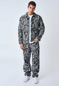 Set di giacca e pantaloni in denim a strisce bianche e nere, caratterizzato da una vestibilità rilassata e un tessuto texturizzato, indossato con una maglietta bianca e sneakers bianche.