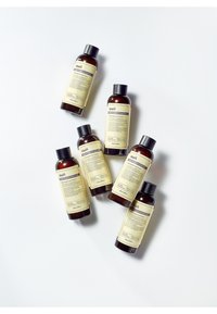 Six bouteilles en ambre de produits de soin de la peau avec des bouchons à vis noirs, présentant des étiquettes minimalistes avec du texte de différentes couleurs et détails.