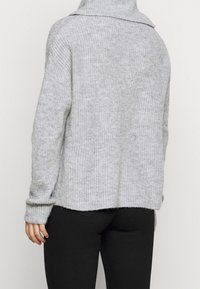 Světlé šedé pletené svetřík s vysokým límcem a dlouhými rukávy, s volným střihem a žebrovanou strukturou. Zadní pohled ukazuje minimální detaily.