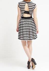 Robe noire et blanche à rayures, avec un corsage ajusté et une jupe évasée, présentant une ouverture à l'arrière et des manches courtes. Portée avec des talons hauts.