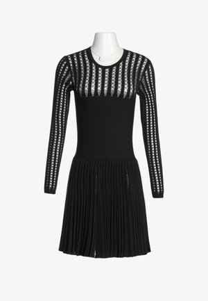 Robe noire à manches longues avec motif à rayures verticales transparentes sur les manches et le haut de la poitrine, taille cintrée et jupe plissée sur un mannequin blanc.