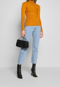 Haut à manches longues et col roulé de couleur moutarde, avec une texture côtelée et des rayures horizontales. Associé à un jean court bleu clair et des bottines noires.