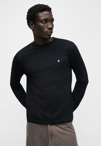 Μαύρο μακρυμάνικο t-shirt από βαμβάκι, με στρογγυλή λαιμόκοψη, εφαρμοστή γραμμή και μικρό λευκό λογότυπο στο στήθος.