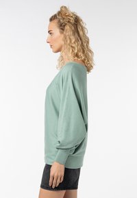 Mintgrüner, übergroßer Pullover mit weitem Ausschnitt und Ballonärmeln, kombiniert mit einem schwarzen Denim-Rock. Weiche Textur und lockere Passform.