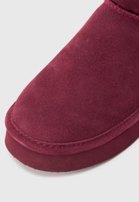 Burgundia nubukist kingad ümarate varvastega ja äärekandiga õmblustega, millel on pehme tekstuur ja minimalistlik disain.