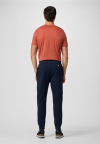 Rode shirt met korte mouwen en marineblauwe joggers. Glad katoen, elastische tailleband, zijzakken, zwarte sneakers met witte zolen.